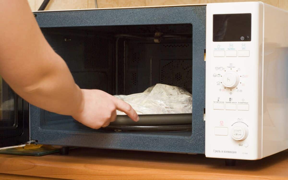 A hand putting a meal covered by a paper tower in a microwave.