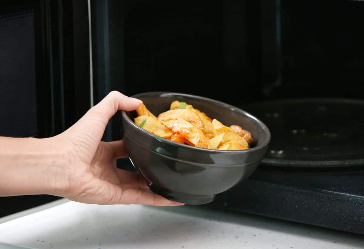 A hand putting a meal in a bowl in a microwave.