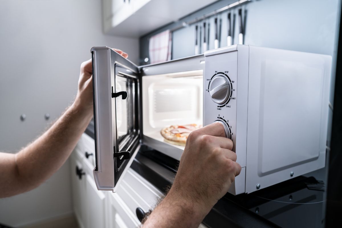 A man setting up a microwave to heat up a pizza.