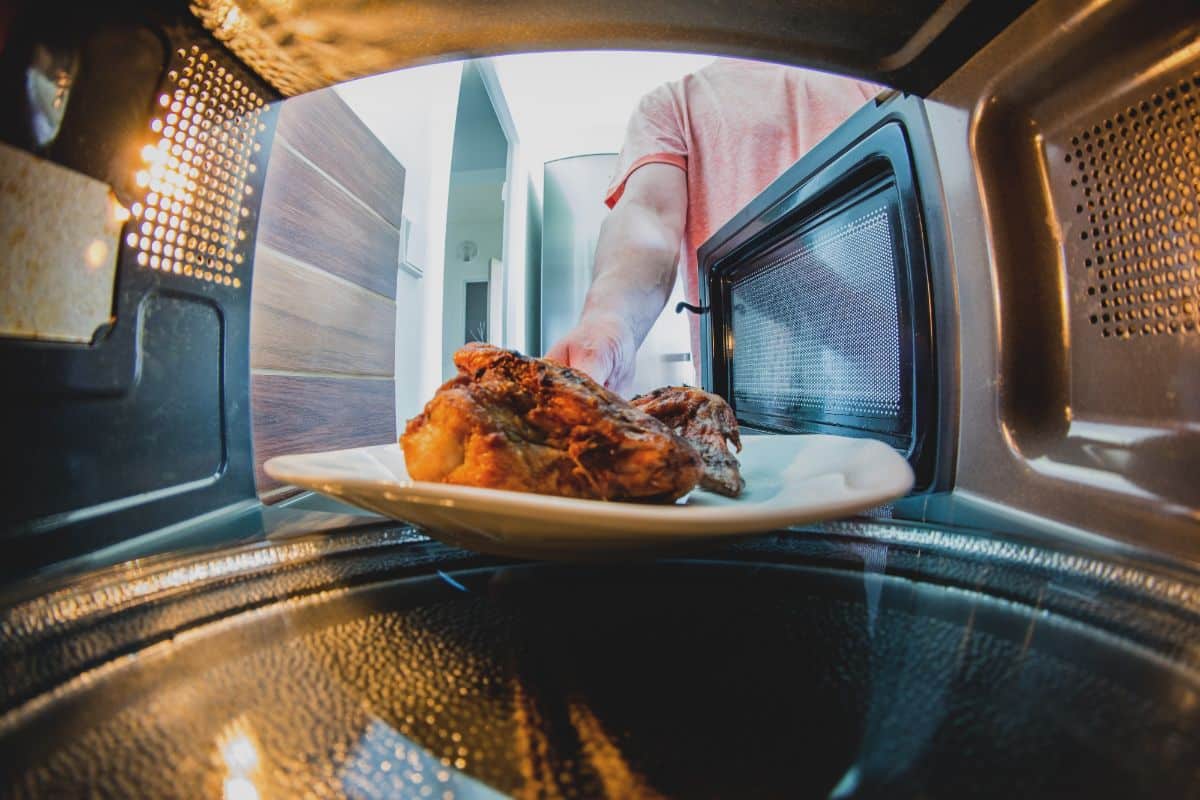 A human putting a meal on a white plate in a microwave.