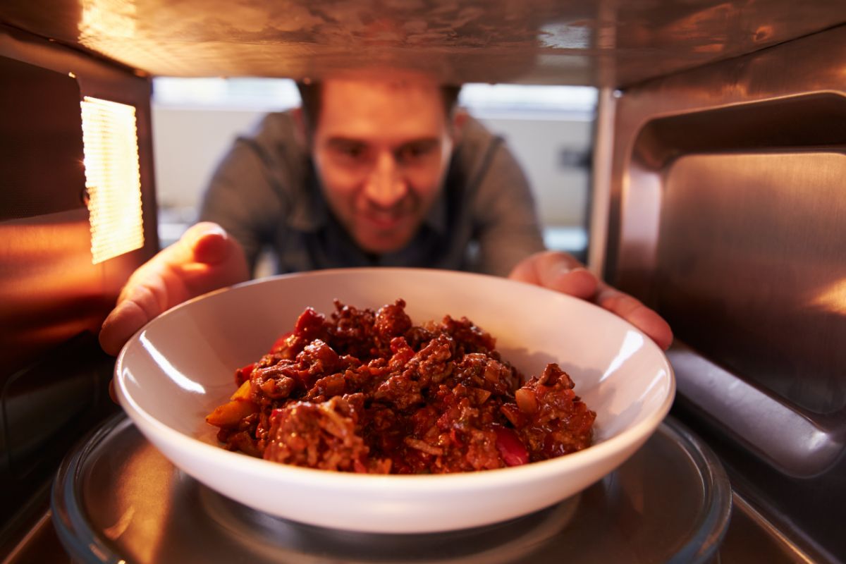 A man putting leftovers on a white plate in a microwave.