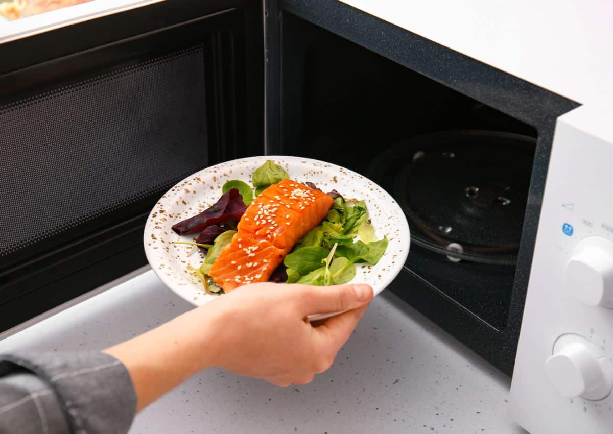 A hand putting up a meal on a plate in a microwave.
