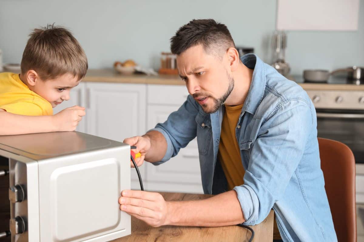 A dad repairing a microwave with a son.