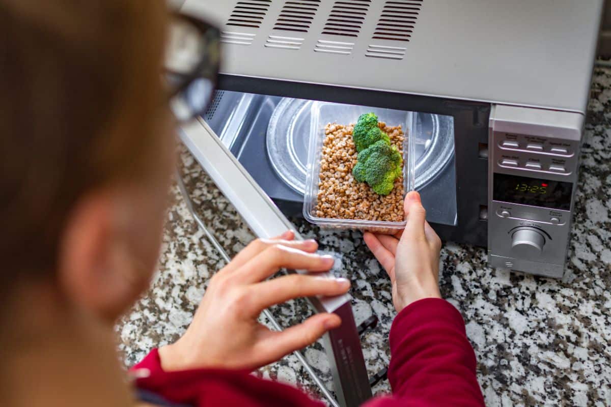 A woman putting a meal in a plastic container in a microwave.