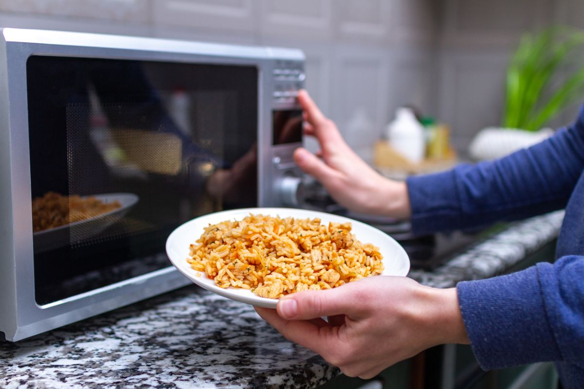 A man holding a meal on a white plate and setting up a microwave.