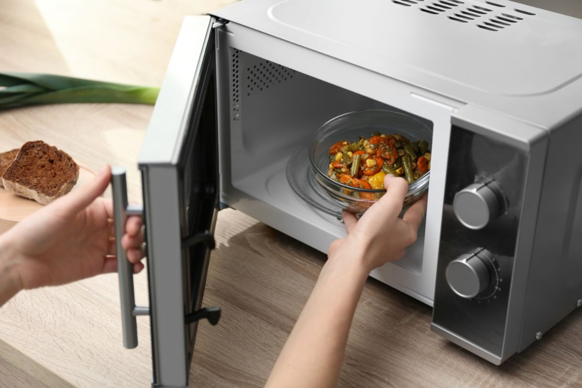 A hand putting up a meal in a bowl in a microwave.