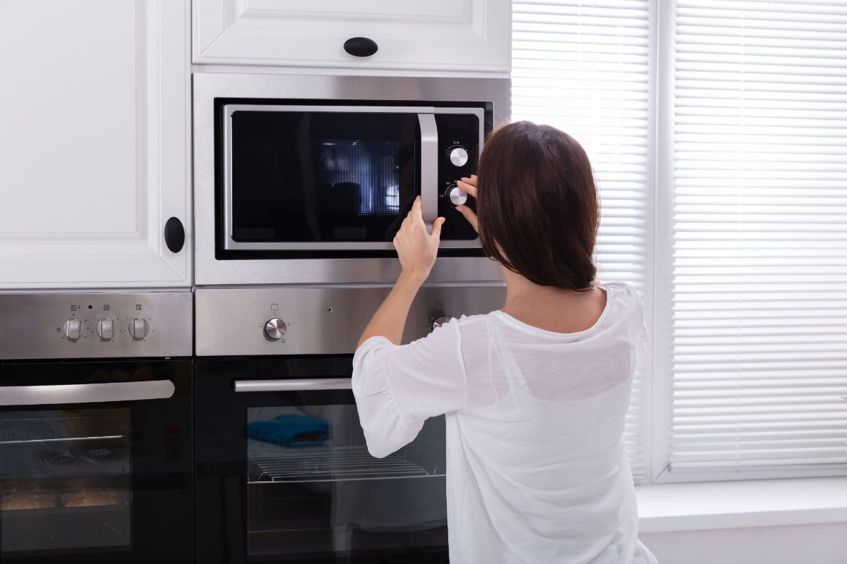 A young woman operating a microwave in a kitchen.