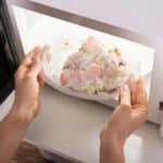 Hands putting a frozen meal in a glass container in a microwave.