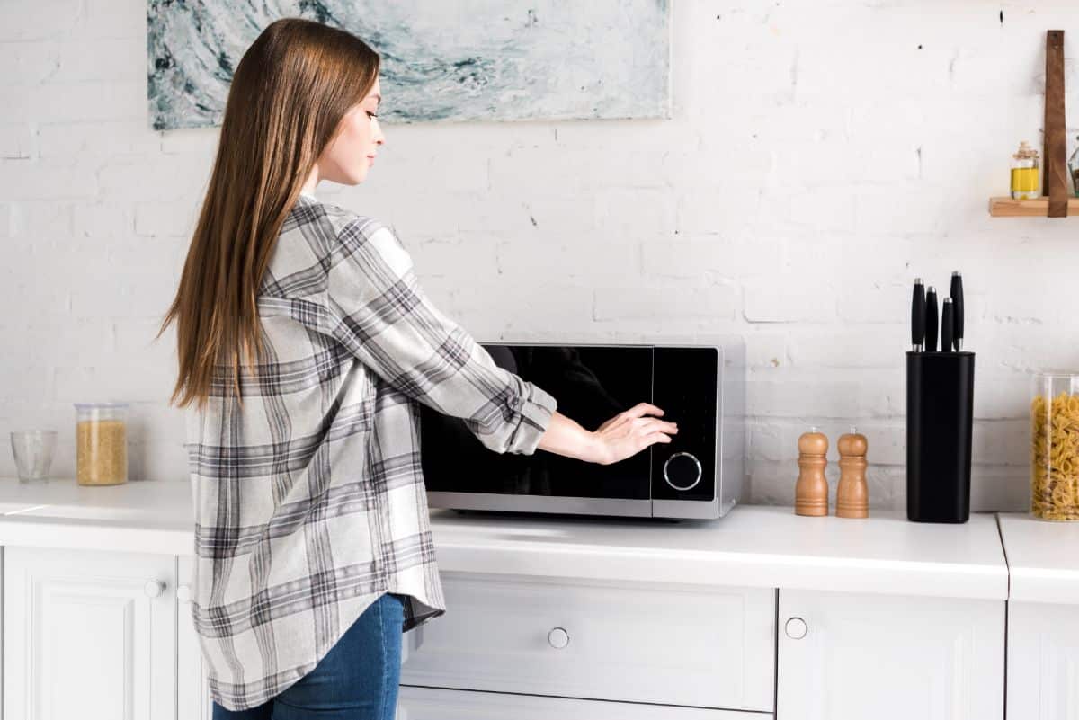 A young woman in a kitchen near a microwave.